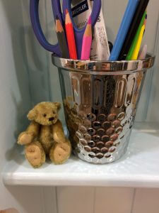 A teddy bear next to a tub of pencils